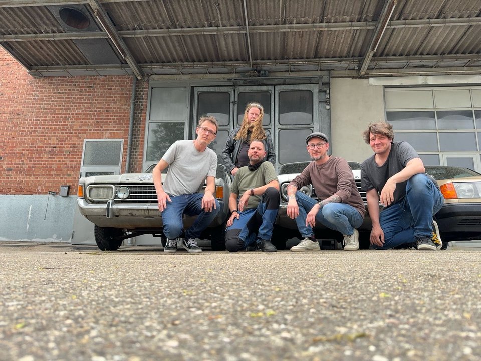 Die fünf STOPPE-Musiker gemeinsam vor einer Industriehalle und zwei Autos
